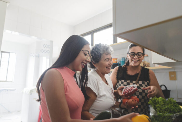 Three smiling Latina women preparing a meal in the kitchen.
